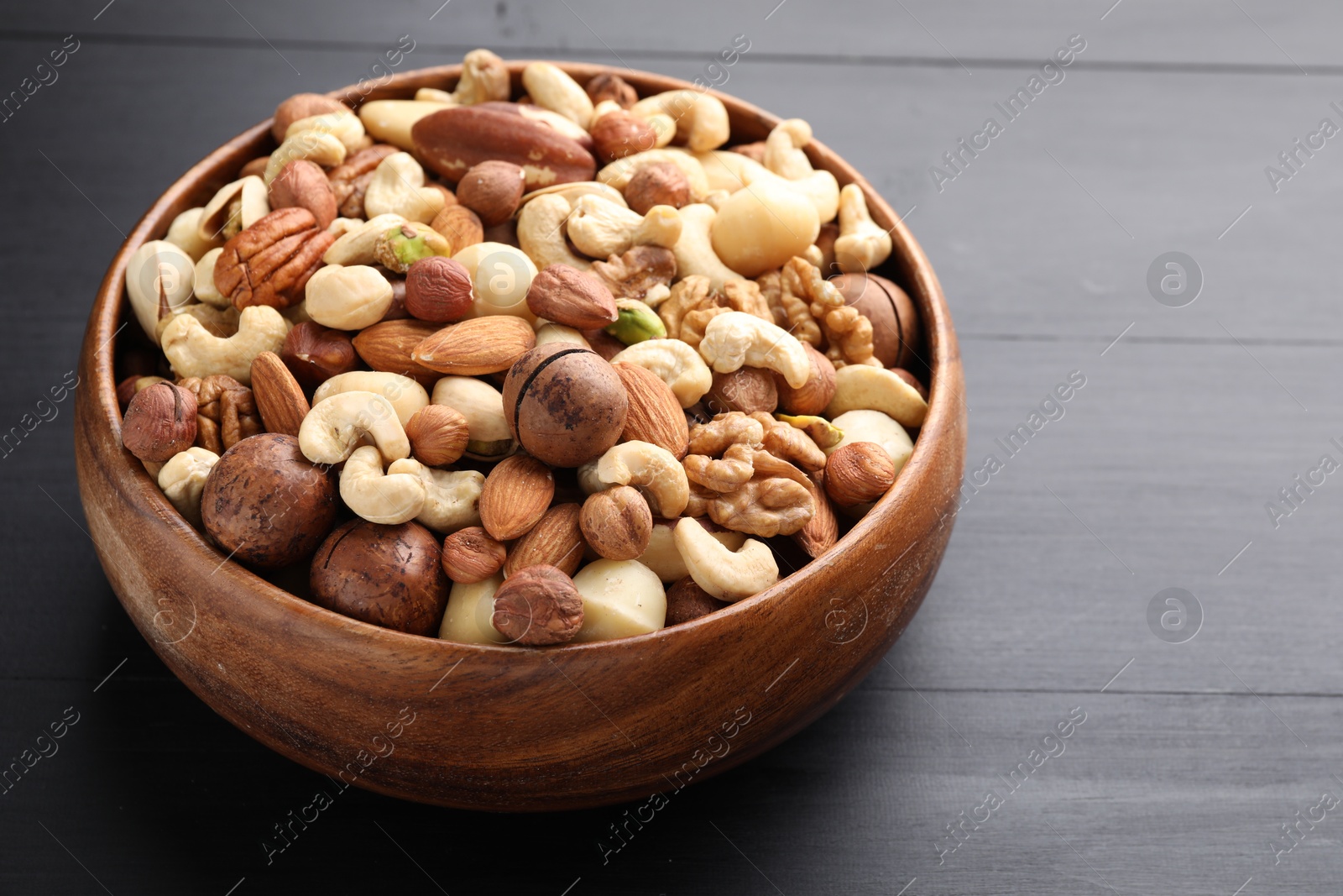Photo of Mix of different nuts in bowl on black wooden table, closeup. Space for text