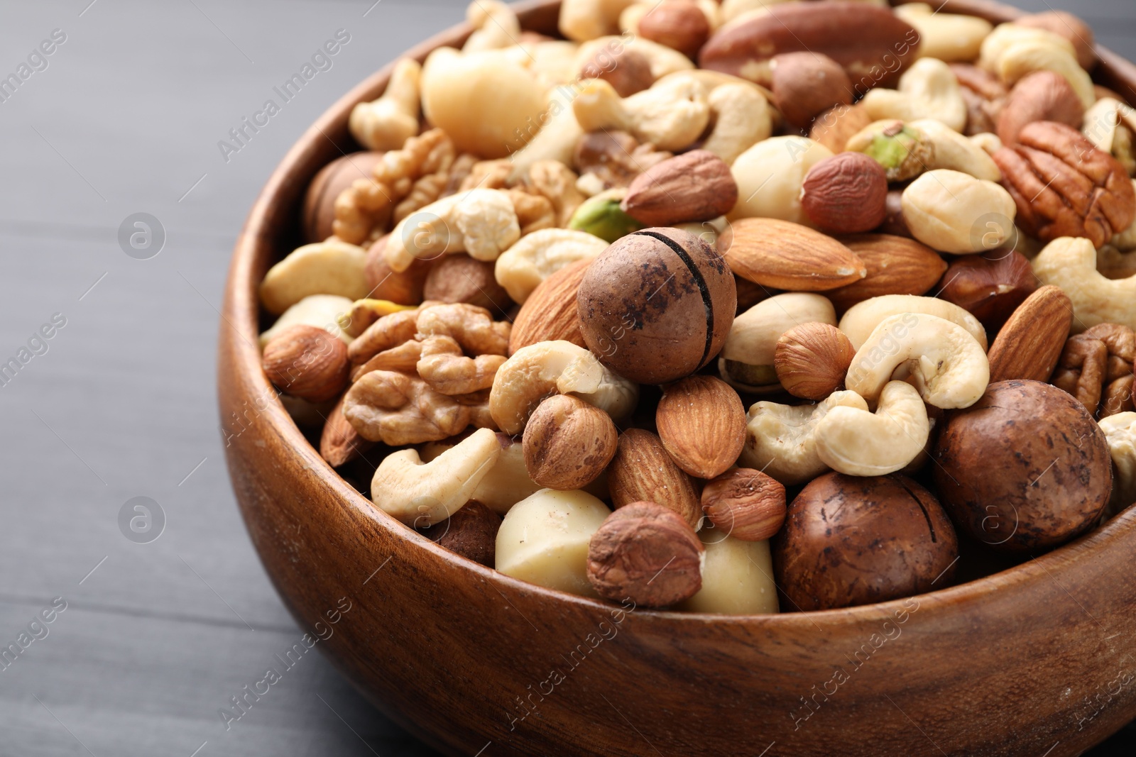 Photo of Mix of different nuts in bowl on black wooden table, closeup