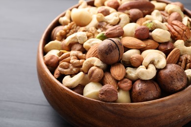 Photo of Mix of different nuts in bowl on black wooden table, closeup