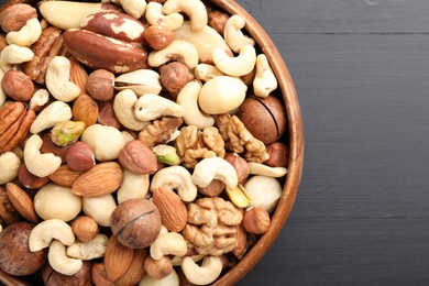 Photo of Mix of different nuts in bowl on black wooden table, top view. Space for text
