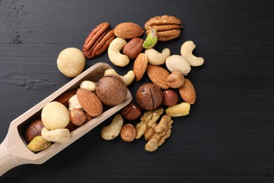 Photo of Mix of different nuts and scoop on black wooden table, flat lay. Space for text