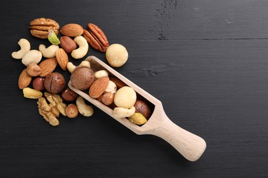 Photo of Mix of different nuts and scoop on black wooden table, flat lay. Space for text
