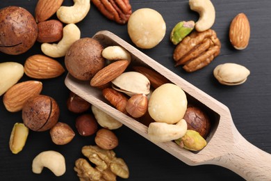 Photo of Mix of different nuts and scoop on black wooden table, flat lay