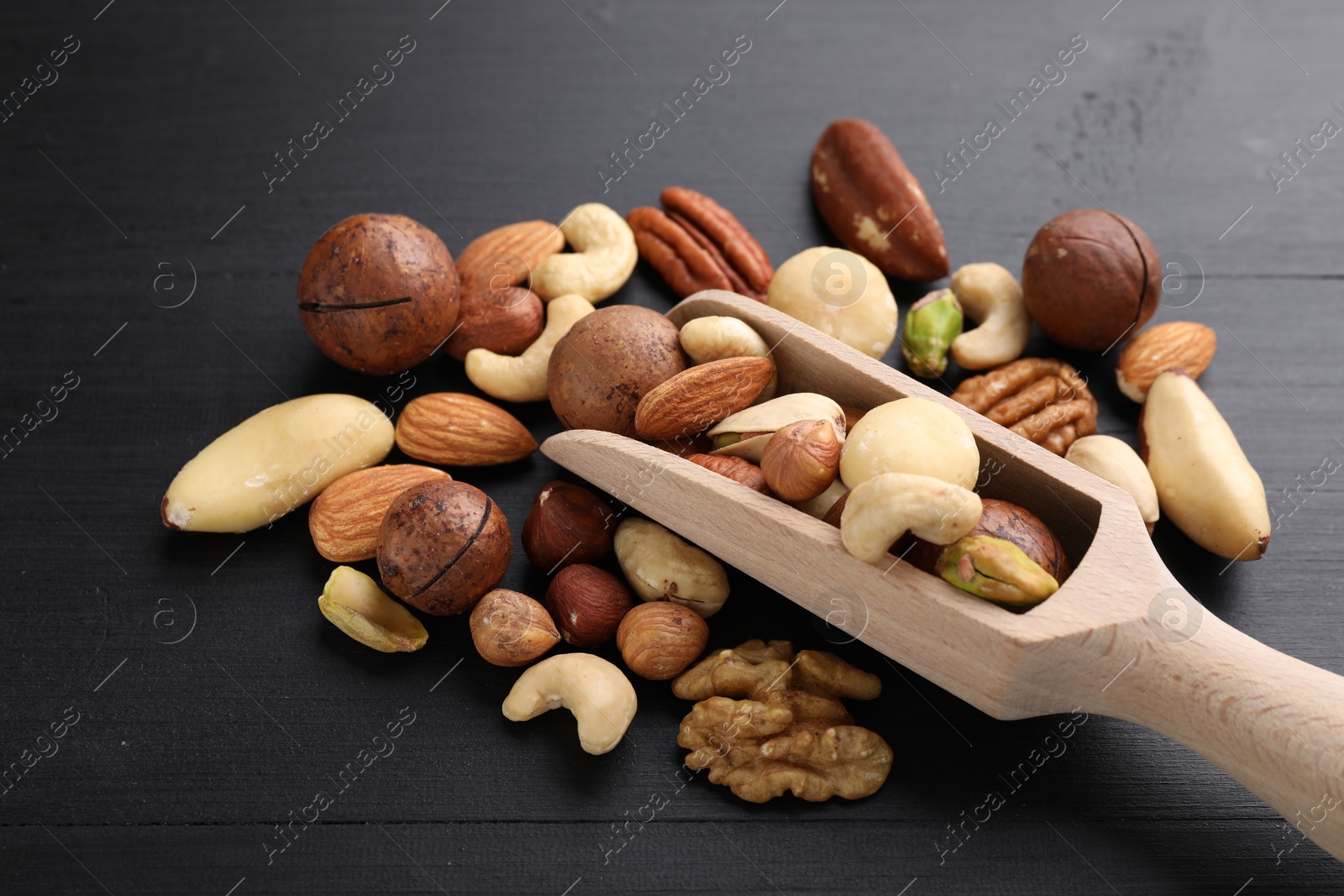 Photo of Mix of different nuts and scoop on black wooden table, closeup