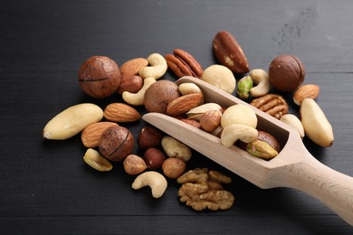 Photo of Mix of different nuts and scoop on black wooden table, closeup