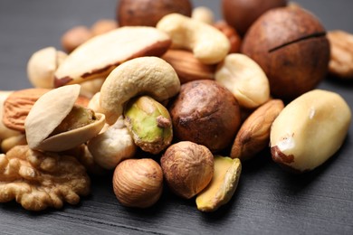Photo of Mix of different nuts on black wooden table, closeup