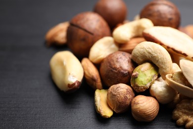 Photo of Mix of different nuts on black wooden table, closeup. Space for text