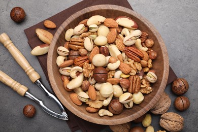 Photo of Mix of different nuts in bowl and nutcracker on grey table, flat lay