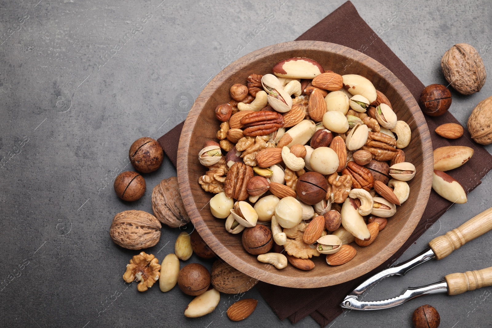 Photo of Mix of different nuts in bowl and nutcracker on grey table, flat lay. Space for text