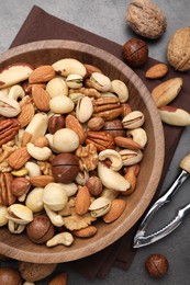 Photo of Mix of different nuts in bowl and nutcracker on grey table, flat lay