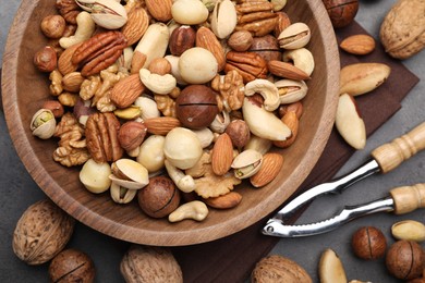 Photo of Mix of different nuts in bowl and nutcracker on grey table, flat lay