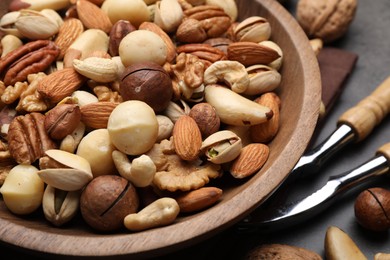 Photo of Mix of different nuts in bowl and nutcracker on grey table, closeup