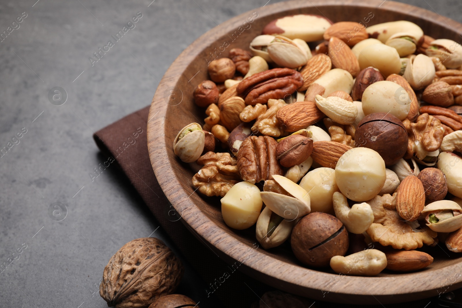 Photo of Mix of different nuts in bowl on grey table, closeup. Space for text
