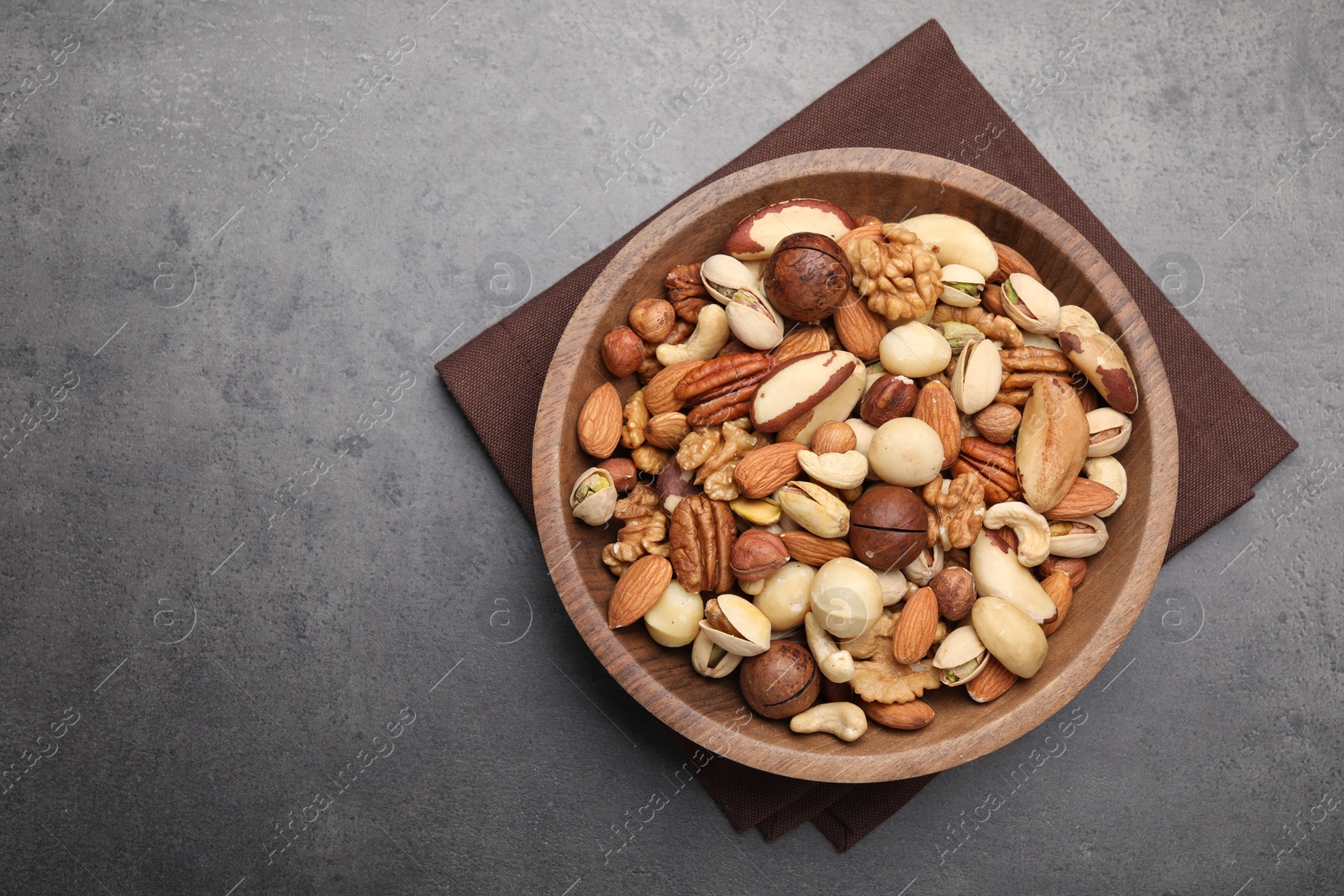 Photo of Mix of different nuts in bowl on grey table, top view. Space for text