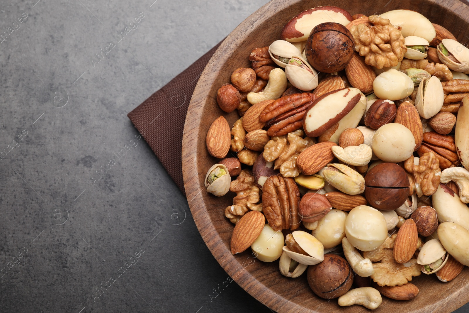 Photo of Mix of different nuts in bowl on grey table, top view. Space for text