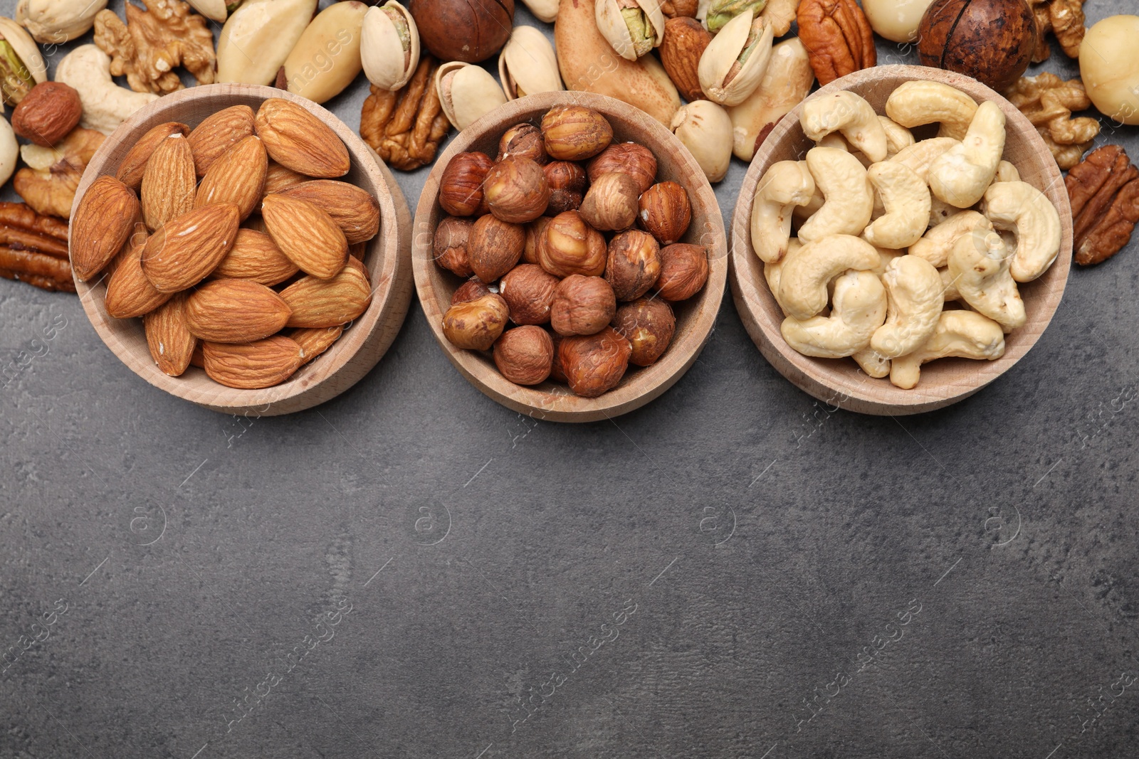 Photo of Mix of different nuts in bowls on grey table, flat lay. Space for text