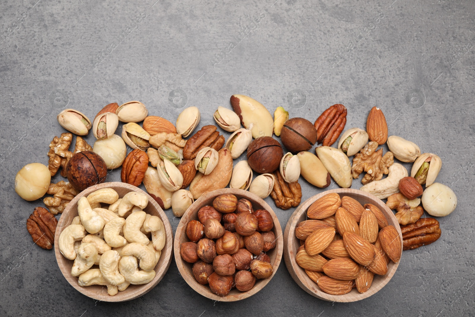 Photo of Mix of different nuts in bowls on grey table, flat lay. Space for text