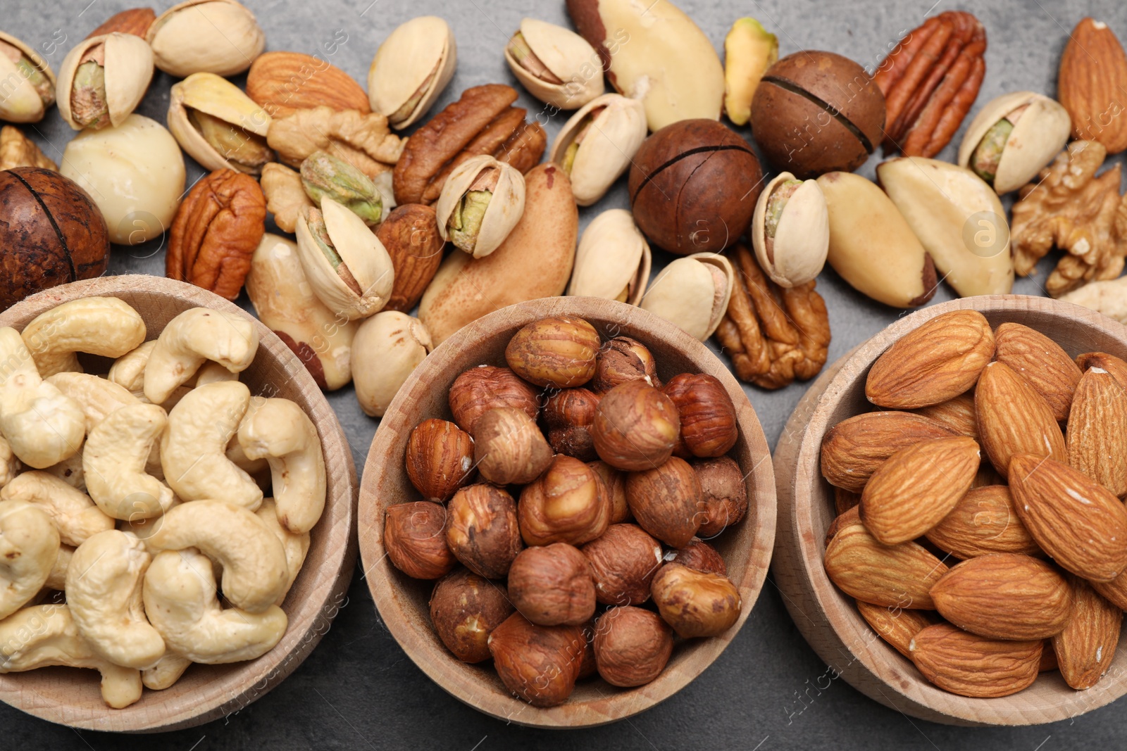Photo of Mix of different nuts in bowls on grey table, flat lay
