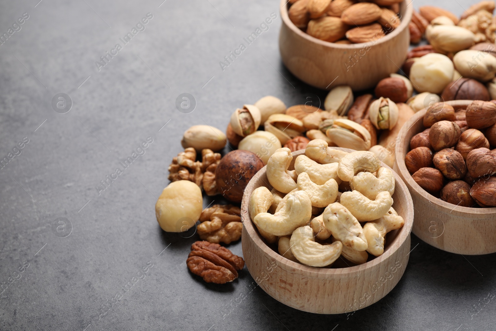 Photo of Mix of different nuts in bowls on grey table, closeup. Space for text