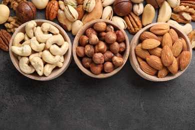 Photo of Mix of different nuts in bowls on grey table, flat lay. Space for text
