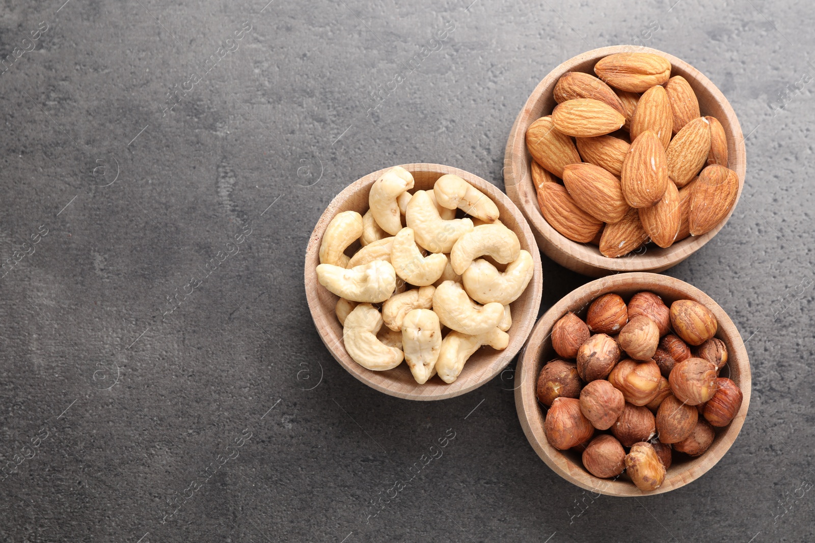Photo of Different nuts in bowls on grey table, flat lay. Space for text