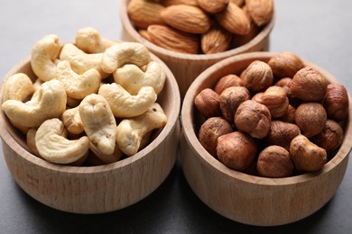 Photo of Different nuts in bowls on grey table, closeup