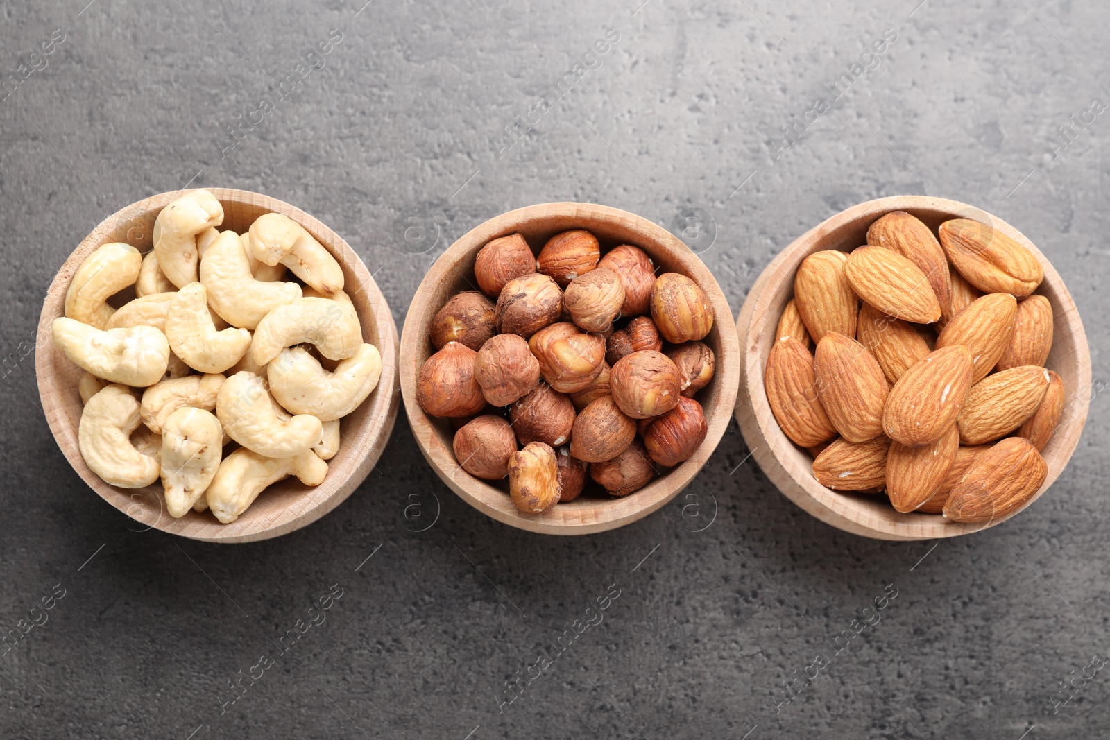 Photo of Different nuts in bowls on grey table, flat lay