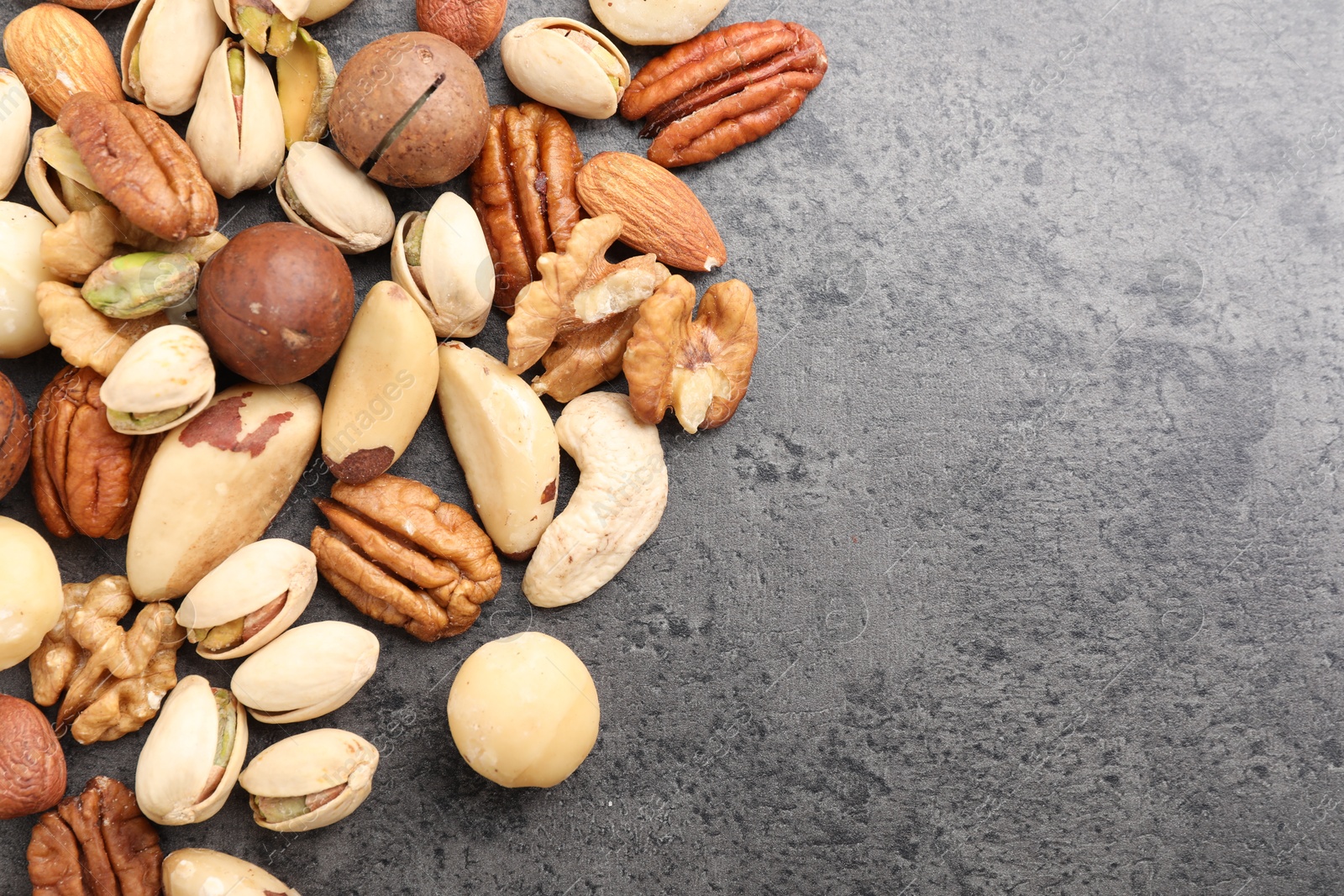 Photo of Mix of different nuts on grey table, flat lay. Space for text