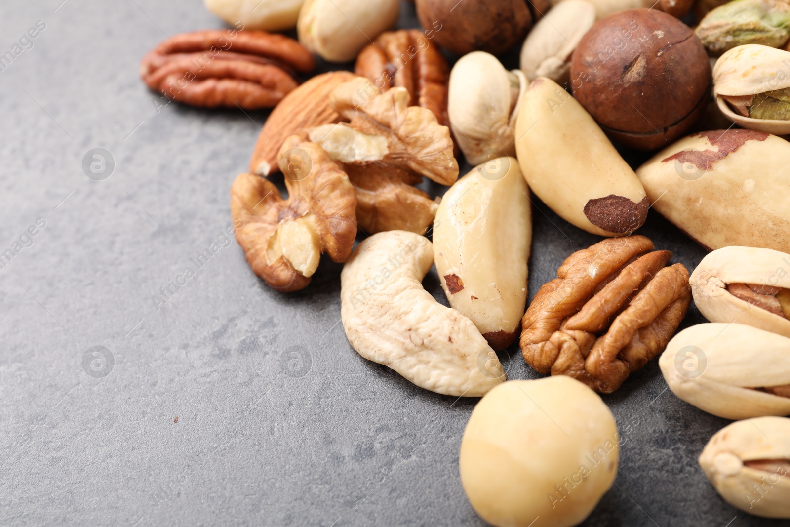 Photo of Mix of different nuts on grey table, closeup. Space for text
