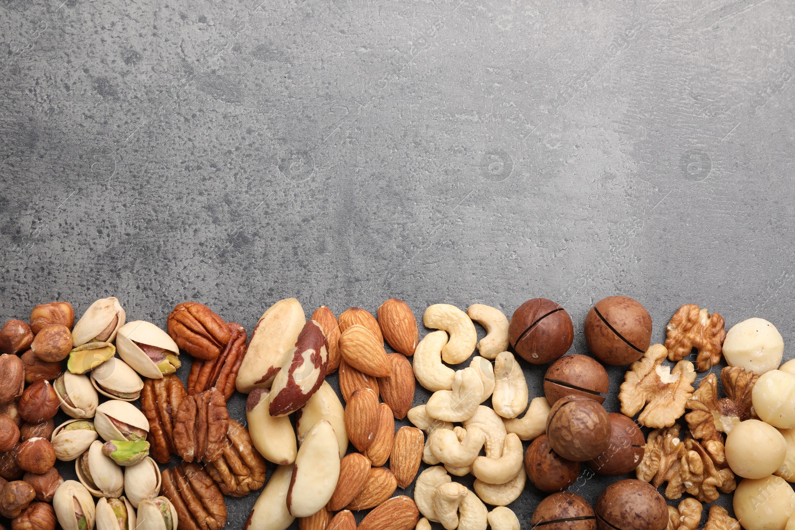 Photo of Mix of different nuts on grey table, flat lay. Space for text