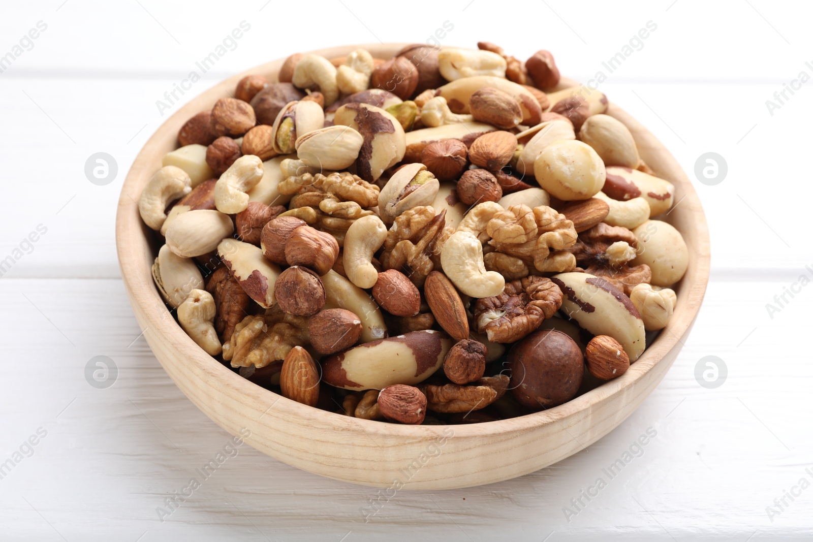 Photo of Mix of different nuts in bowl on white wooden table, closeup