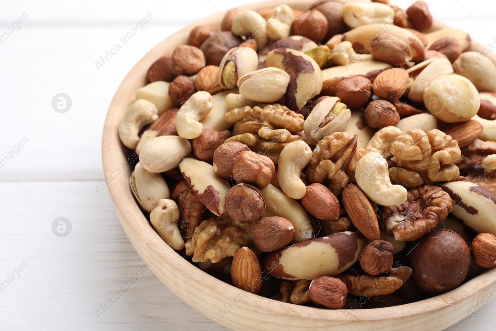Photo of Mix of different nuts in bowl on white wooden table, closeup