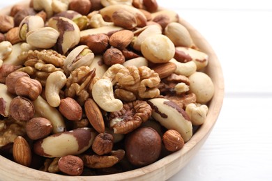 Photo of Mix of different nuts in bowl on white wooden table, closeup