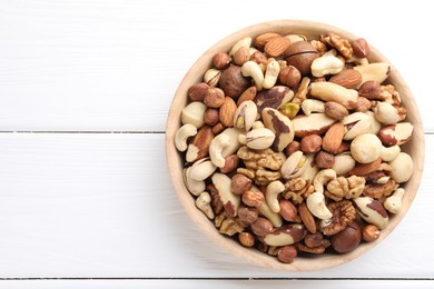 Photo of Mix of different nuts in bowl on white wooden table, top view. Space for text