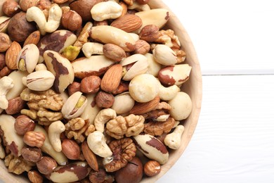 Photo of Mix of different nuts in bowl on white wooden table, top view. Space for text