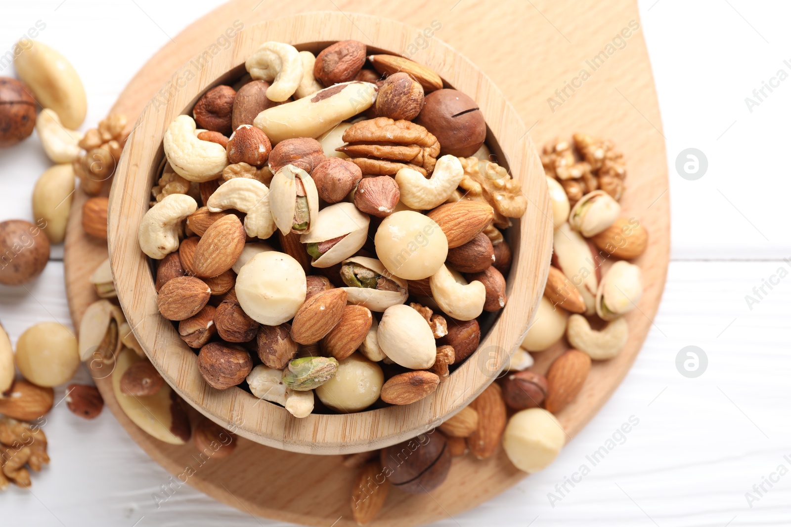 Photo of Mix of different nuts in bowl on white wooden table, top view