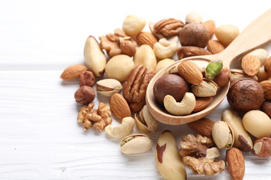 Photo of Mix of different nuts and spoon on white wooden table, closeup. Space for text