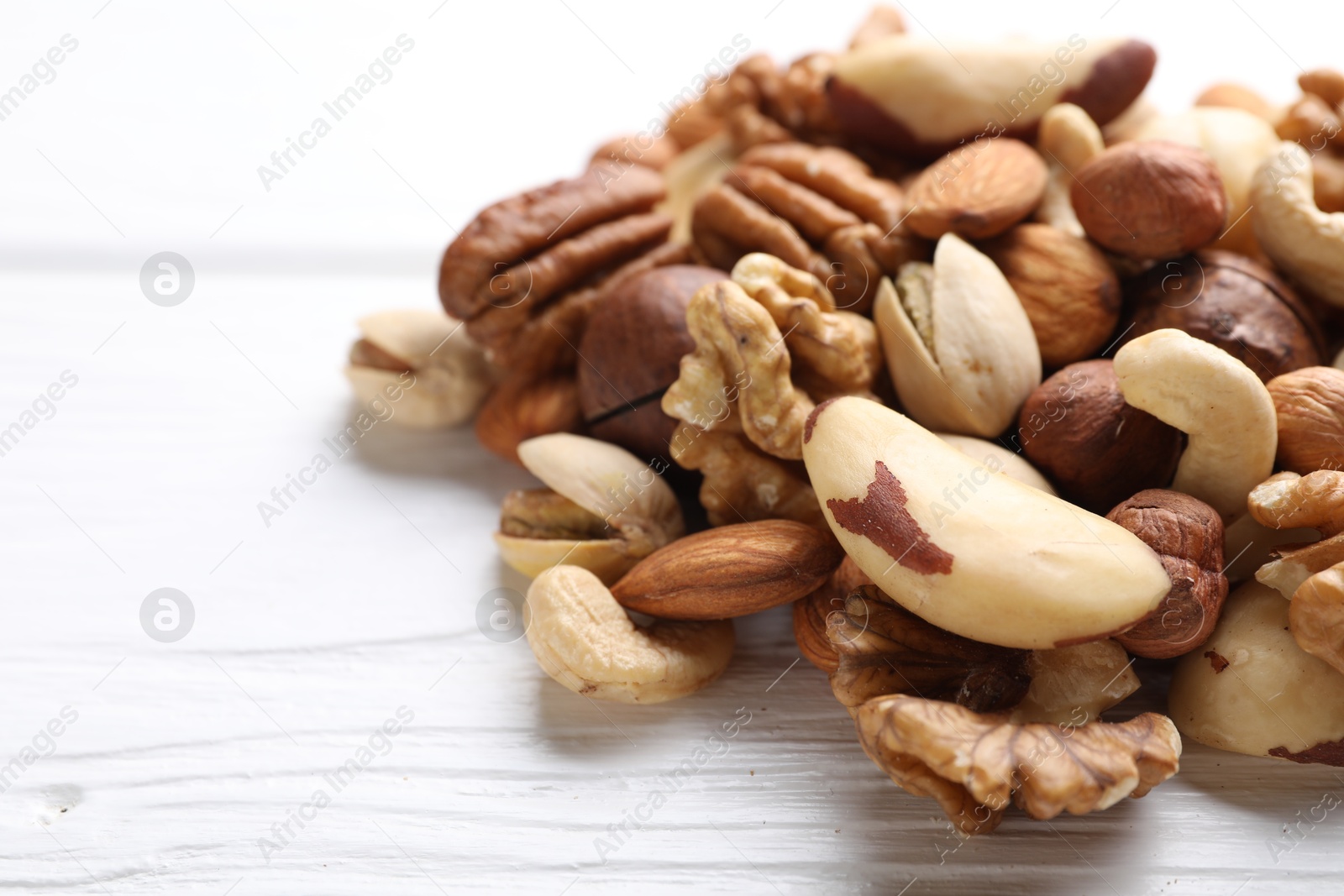 Photo of Mix of different nuts on white wooden table, closeup. Space for text