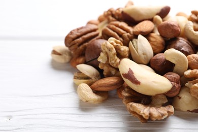 Photo of Mix of different nuts on white wooden table, closeup. Space for text