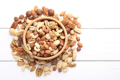 Photo of Mix of different nuts in bowl on white wooden table, flat lay. Space for text