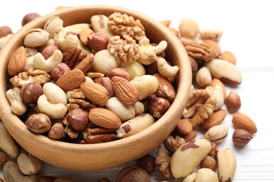 Photo of Mix of different nuts in bowl on white wooden table, closeup