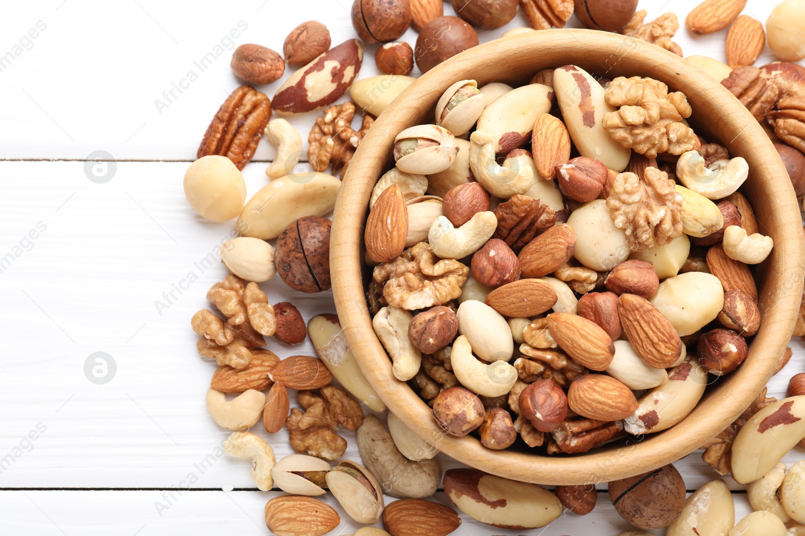 Photo of Mix of different nuts in bowl on white wooden table, flat lay. Space for text