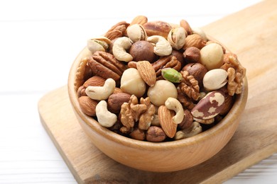 Photo of Mix of different nuts in bowl on white wooden table, closeup