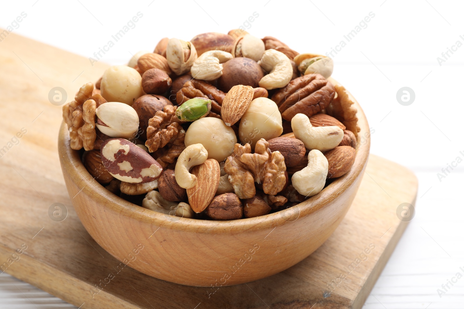 Photo of Mix of different nuts in bowl on white wooden table, closeup