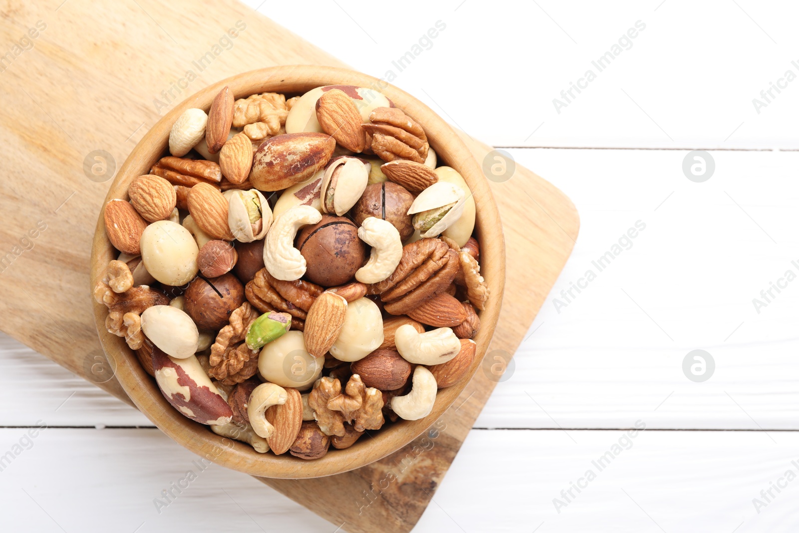 Photo of Mix of different nuts in bowl on white wooden table, top view. Space for text