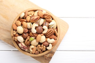 Photo of Mix of different nuts in bowl on white wooden table, top view. Space for text