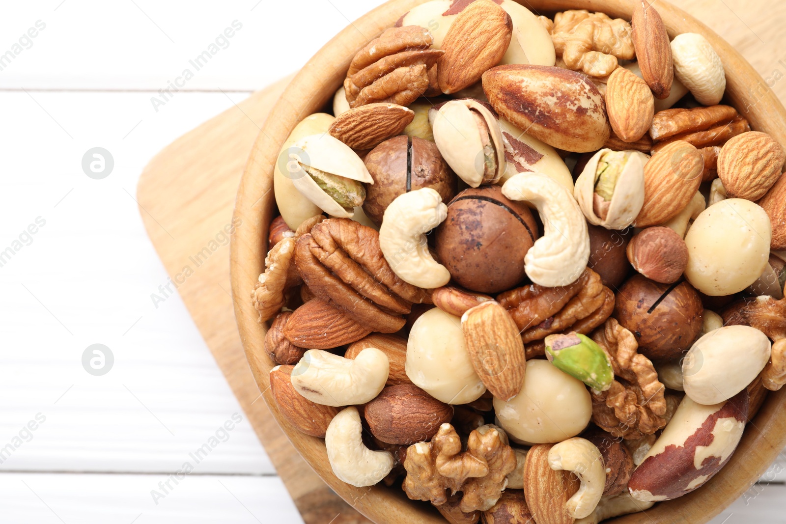 Photo of Mix of different nuts in bowl on white wooden table, top view. Space for text