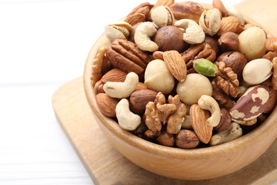 Photo of Mix of different nuts in bowl on white table, closeup. Space for text