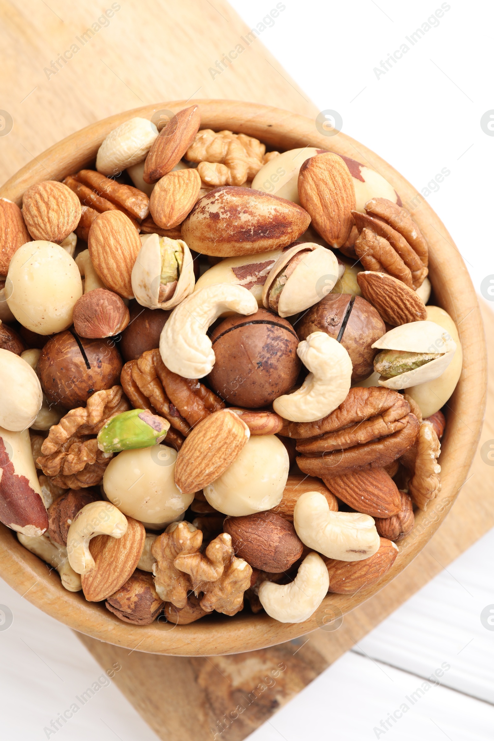 Photo of Mix of different nuts in bowl on white wooden table, top view