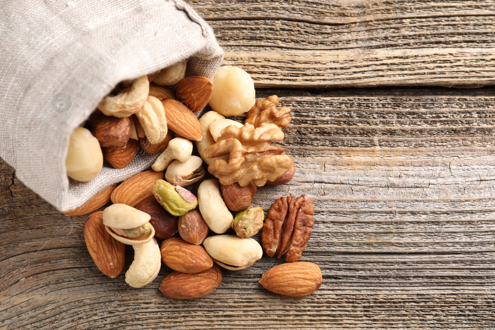 Photo of Mix of different nuts in bag on wooden table, closeup. Space for text
